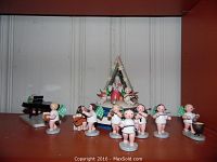 Full set of ten angel figurines arranged in front of triangular wooden music box on white beadboard background