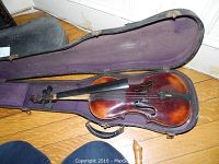 Violin inside open hard case with purple velvet lining, showing reddish-brown varnish body, fingerboard, and scroll visible.