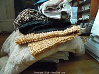 Stack of assorted textiles including a thick camel-hair blanket with fringes and layered cloth pieces on top