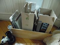 Wooden box holding several cardboard boxes with lighting parts and loose components on the floor near a doorway.