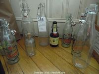 Wide view of all 9 vintage glass bottles arranged on wooden floor, showing variety of shapes, sizes, and stopper types
