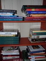 Stacked assortment of cookbooks showing multiple titles and colorful spines on wooden shelf