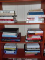 Books arranged on a wooden bookshelf showing approximately 30+ cookbooks stacked horizontally and vertically.