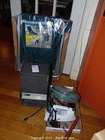 Full view of all items in the lot including backpack beach chair in packaging, black dehumidifier unit, white curling iron, white steam iron, hair dryer, and neck pillow.