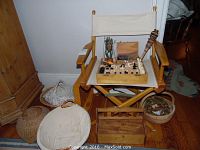 Danish collapsible director's chair with cream canvas seat and back, surrounding baskets, and chess set boxes on seat.