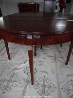 Front leg and edge of round mahogany table showing wood grain and damage on one leg and wear on the leaf.