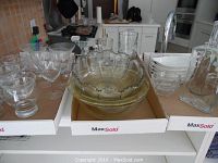 Assorted glassware on a white shelf including cocktail glasses, bowls, decanter and salad dishes, showing quantity and variety.
