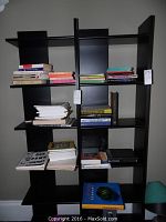 Overview of multiple books stacked on a black shelving unit, showing volume and variety of book types.
