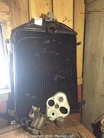 Cast‐iron radiator leaning against wooden wall; dash panel and carburetor on bench in front
