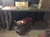 Work table with metal legs and wood top, press underneath with wheels visible.
