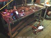 Full view of metal work table with various tools on top and items beneath the table.