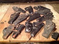 Full assortment of black leather holsters and one plastic speedloader displayed on wood table.