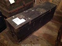 Closed solid wood trunk with black painted exterior and visible wear marks, size dimensions note on top 44x11x18 inches.