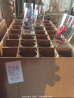 Box containing 28 glass drinking glasses, each with a different 1980s NFL team logo and helmet print