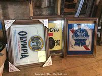 Six vintage framed beer and beverage signs on wooden surface, showing front designs including Olympia, Coors, and Pabst Blue Ribbon.