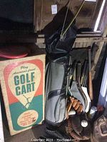 Boxed vintage golf cart, golf bag with clubs, baseball gloves with balls, and other sports equipment stored in a wooden shed.