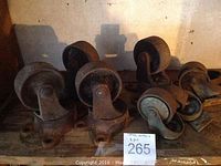 Eight metal casters arranged in two matched sets of four, showing heavy rust and wear.