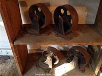 Four heavy cast iron casters on wooden shelf, showing rust and wear, arranged in pairs