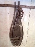 Pair of vintage wooden and rawhide snow shoes hanging on a wall, showing full front profile of frames and bindings.