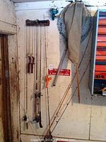 Fishing poles, two fishing nets hanging on white wall, some poles with reels and worn handles