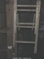 Photo showing partially retracted aluminum extension ladder placed vertically against wooden structure.