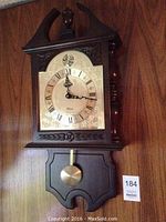 Full view of the wood Bulova wall clock with decorative carved top and lower section, dial with Roman numerals, and brass pendulum.