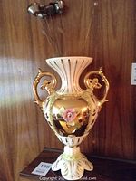 Porcelain vase with gold detailing and pink rose decoration shown from front angle.