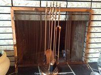 View of copper coloured fireplace tool set standing in front of matching fireplace screen framing a stone fireplace.