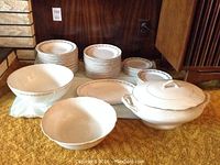 Full set of stacked white china with gold floral trim including plates, bowls, tureen, and serving dishes
