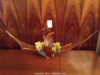 Front view of amber-colored decorative glass sculpture with long tapering ends and central abstract shape on wooden surface.