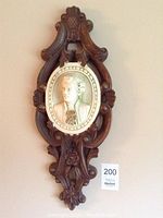 Full view of one decorative wall art piece showing the carved wood frame and oval classical portrait