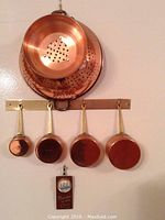 Copper hanging kitchenware including colanders and ladles on a wall-mounted rack