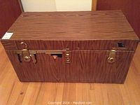 Front view of steamer trunk showing wood print shelf paper covering with peeling, metal latches and keyhole