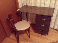 Vintage wood desk and chair set in a room with wood flooring and curtains. Desk has three drawers on the right side with metal handles.