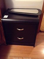 Photo of black wood night table with two drawers and silver handles, with a small wall mirror placed on top