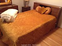 Full view of the vintage wood bed frame with double mattress covered in a golden-brown quilted bedspread and round decorative pillows.