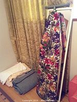 Photo showing folded blankets stacked next to a curtain with floral pattern, including a floral patterned blanket in front.