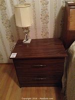 Nightstand with lamp on top, showing dark wood grain finish and metal drawer pulls.