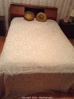 Full view of bed with cream crochet-style bedspread and two round gold decorative pillows