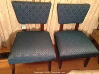 Pair of two vintage 1950s hostess chairs with blue patterned fabric upholstery, trapezoidal backs, and wooden legs.