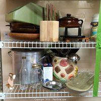 Photo of kitchen shelving showing large stainless steel 16 quart stock pot, glass bottles, jars, a ceramic covered pot, metal bowls, and plastic bakeware dishes.