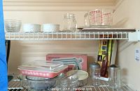 Shelving with a variety of glass and ceramic kitchen items including white ramekins, Pyrex measuring cup, clear glass bowls, and a small mason jar.