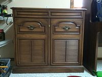 Front view of wooden bar cabinet showing two drawers with brass handles and two louvered doors with central lock.