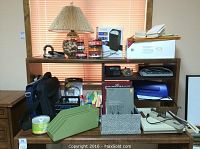 Photo showing multiple office supplies including filing accessories, electronics, and desk lamp on a wooden shelving unit.