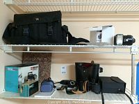 Black camera bag, camera flash, boxes and binoculars on shelves