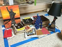 Overview of the lot showing stacks of vintage Playbills, the Statue of Liberty painting, several books or albums, a blue sculpture, and a black lamp with built-in clock on the base.