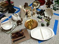 Top view of assorted collectibles including Lenox dish, ceramic swan, camel, vases, figurines, and candle holders arranged on floor with blue tape boundaries.