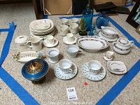 Full view of ceramic dinnerware including cups, bowls, plates, and serving pieces arrayed on floor showing mixed patterns and styles.