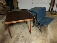Photo showing the folding card table with wood grain top and the vintage painted school desk with attached seat, both shown side by side on concrete floor.