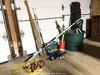 Fishing gear including fishing poles, tackle box, and reels arranged on floor and leaning against garage door.